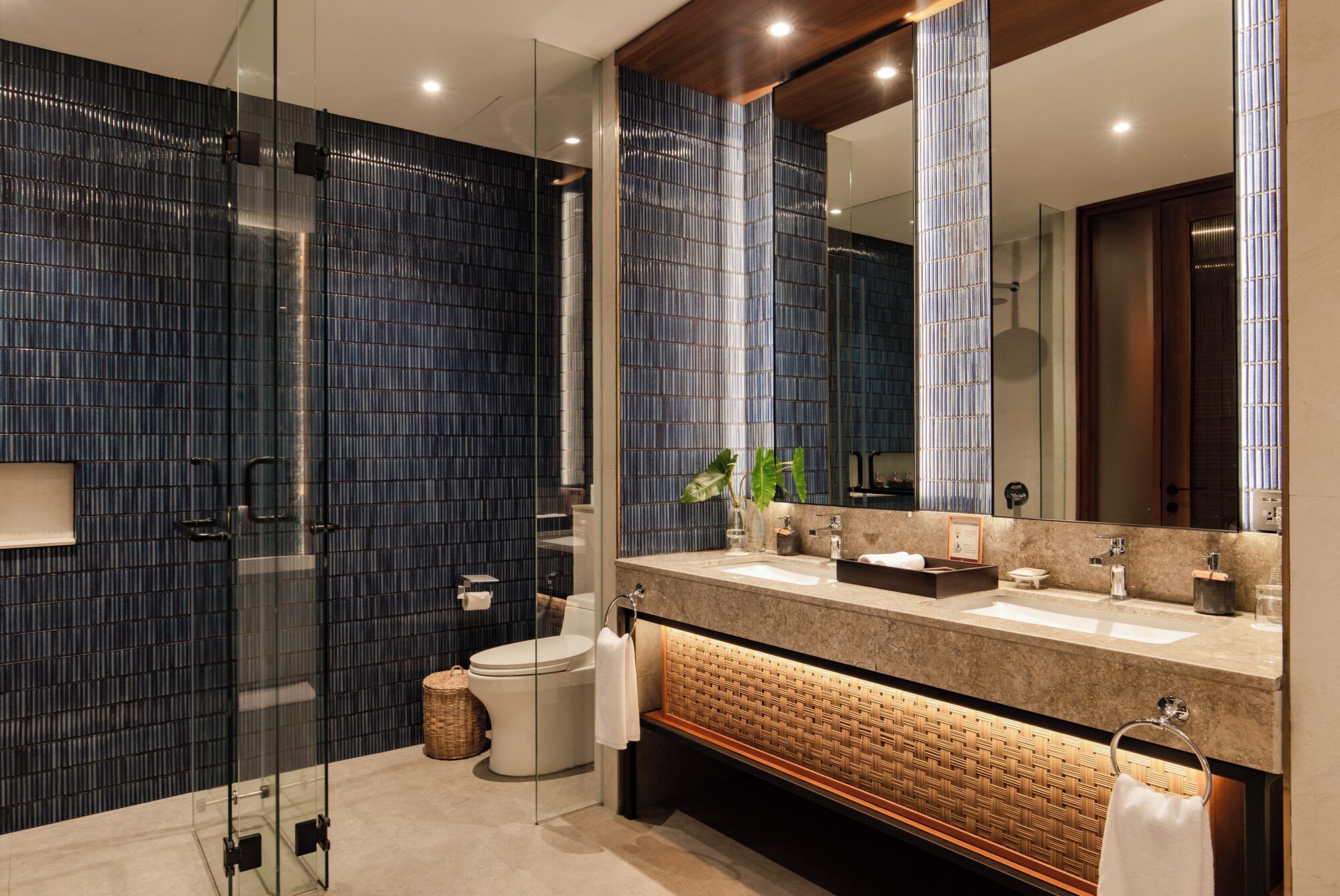 A modern bathroom with a glass shower enclosure, a large mirror, and a vanity with a woven shelf.