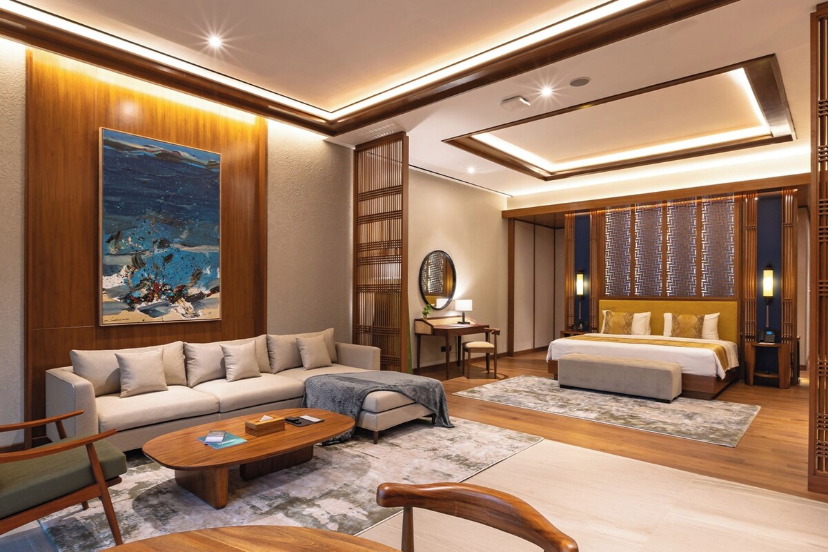 A modern hotel room with a sofa, a bed, a desk, and a large painting.