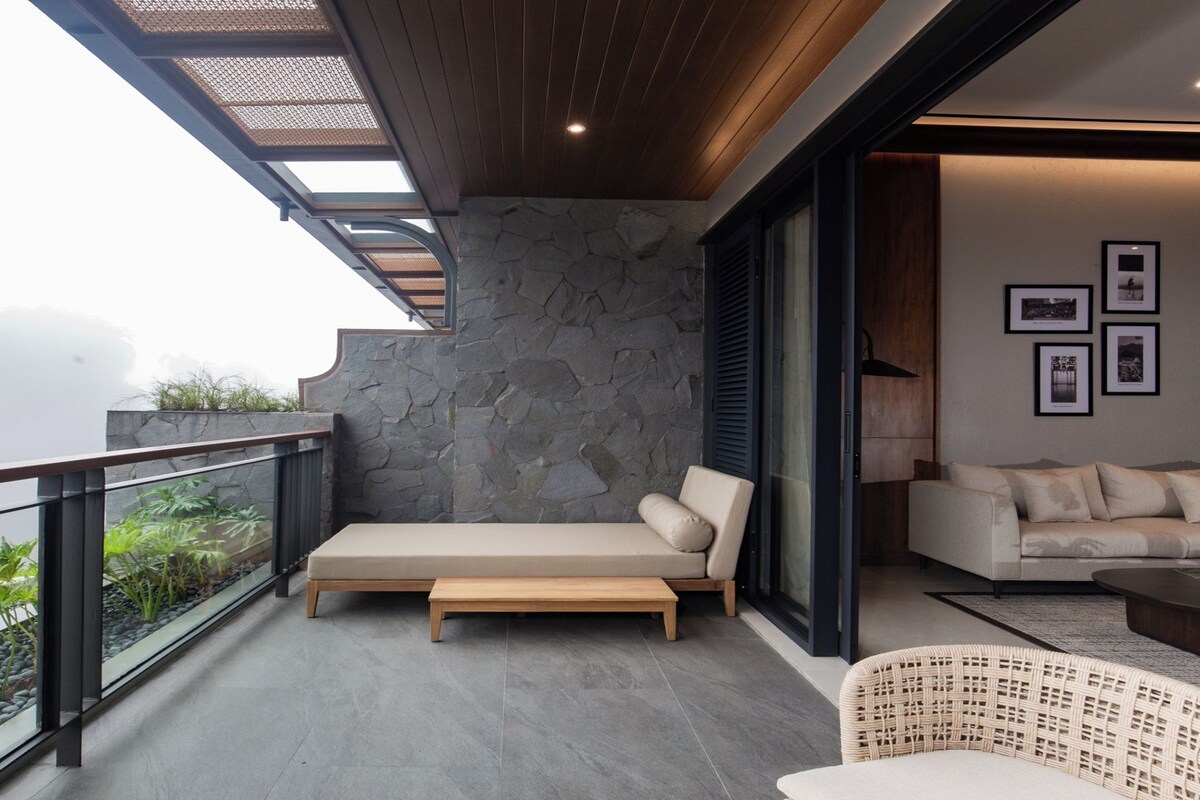 A balcony with a stone wall, a sofa, a wooden bench, and a wicker chair.