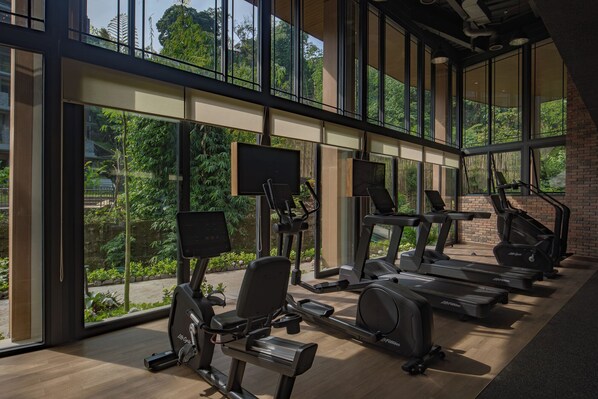 Gimnasio con máquinas de cardio y un amplio ventanal con vistas a zonas verdes.