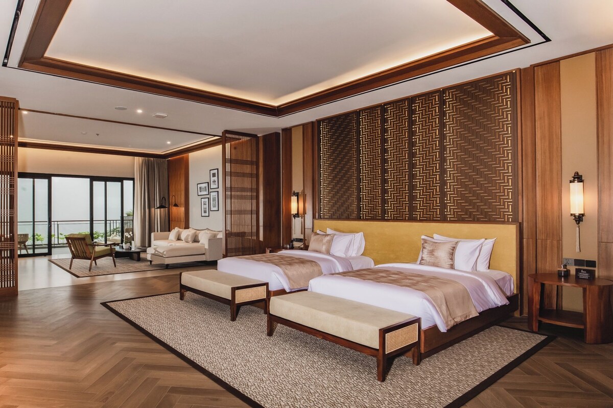 Una habitación de hotel moderna con una cama grande, una zona de estar con sofá y sillones, y vistas a través de una puerta de cristal.