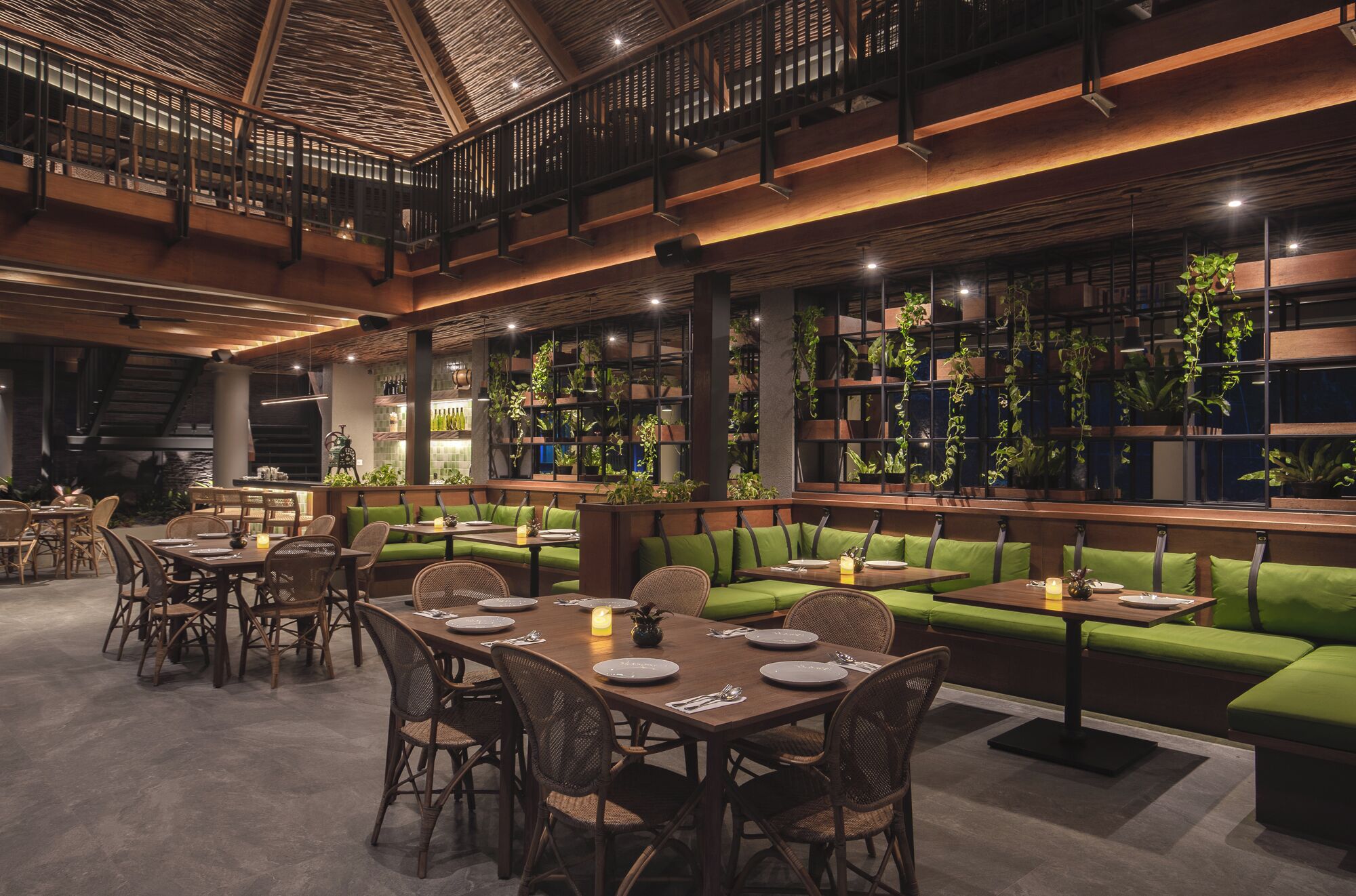 A spacious indoor dining area with high ceilings, wooden beams, and green cushioned seating.