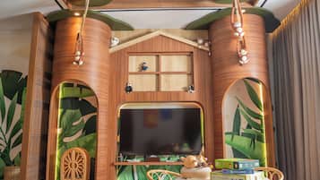 A room with a large flat-screen TV, wooden decor, a small table with items, and a chair.