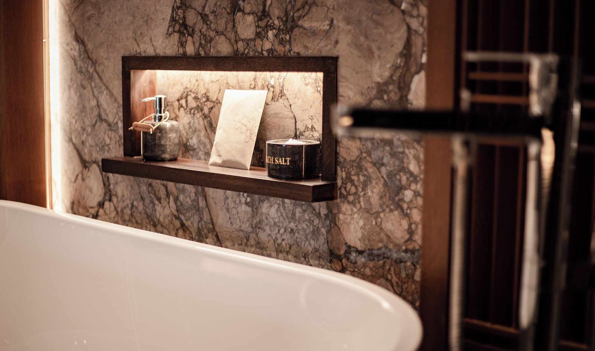 A marble bathroom with a shelf holding a candle, a towel, and a salt container.