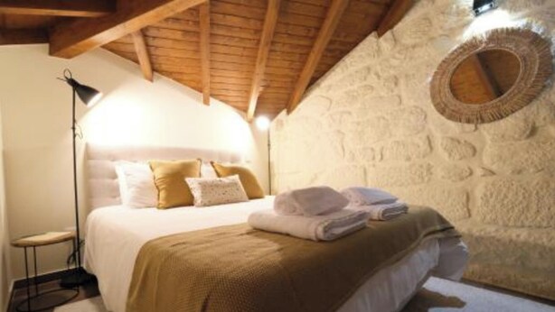 A cozy bedroom with a bed, a bedside lamp, a stone wall, and a circular mirror.