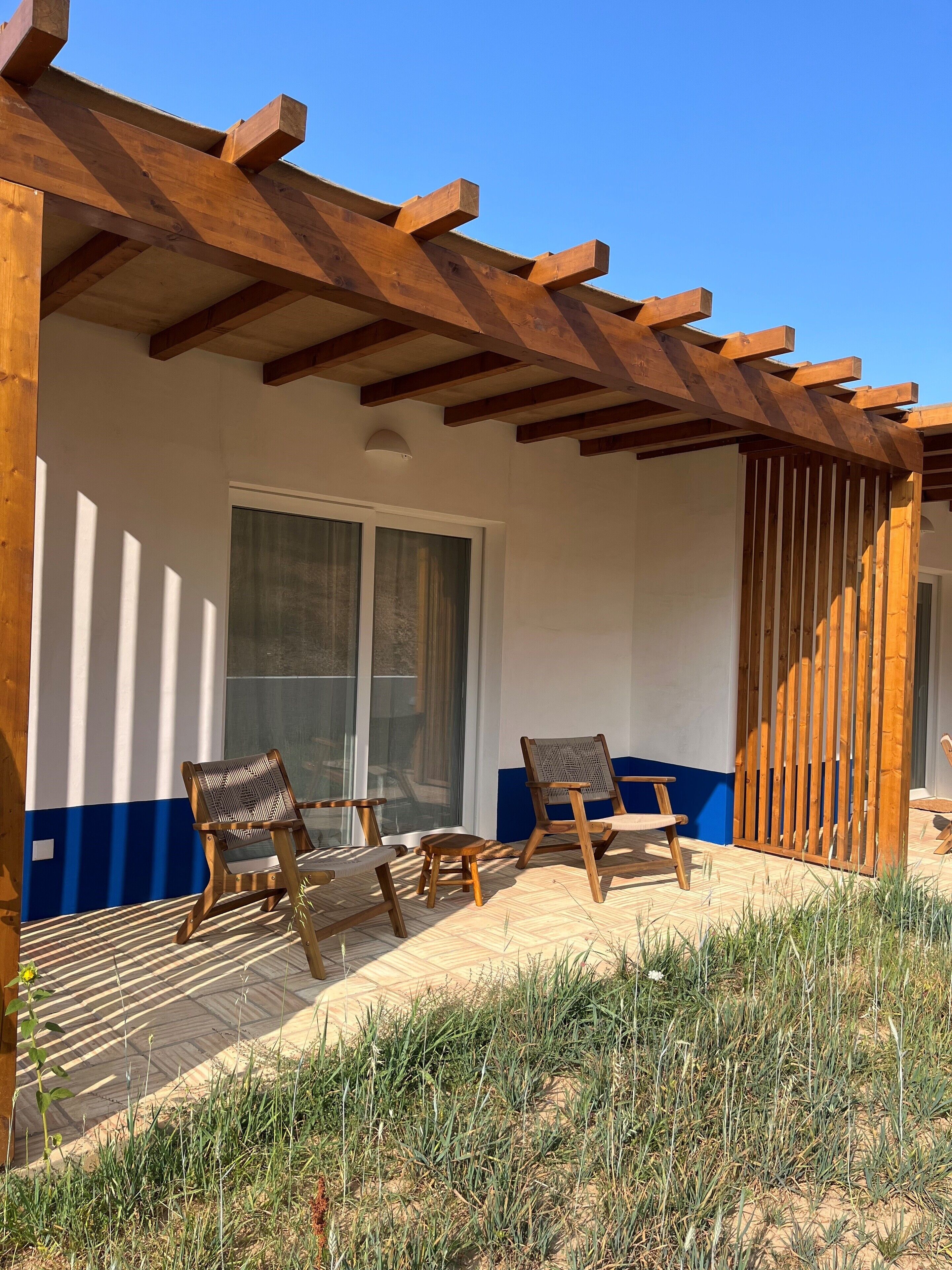 A covered outdoor seating area with wooden chairs and a table, a sliding glass door, and a wooden pergola structure.