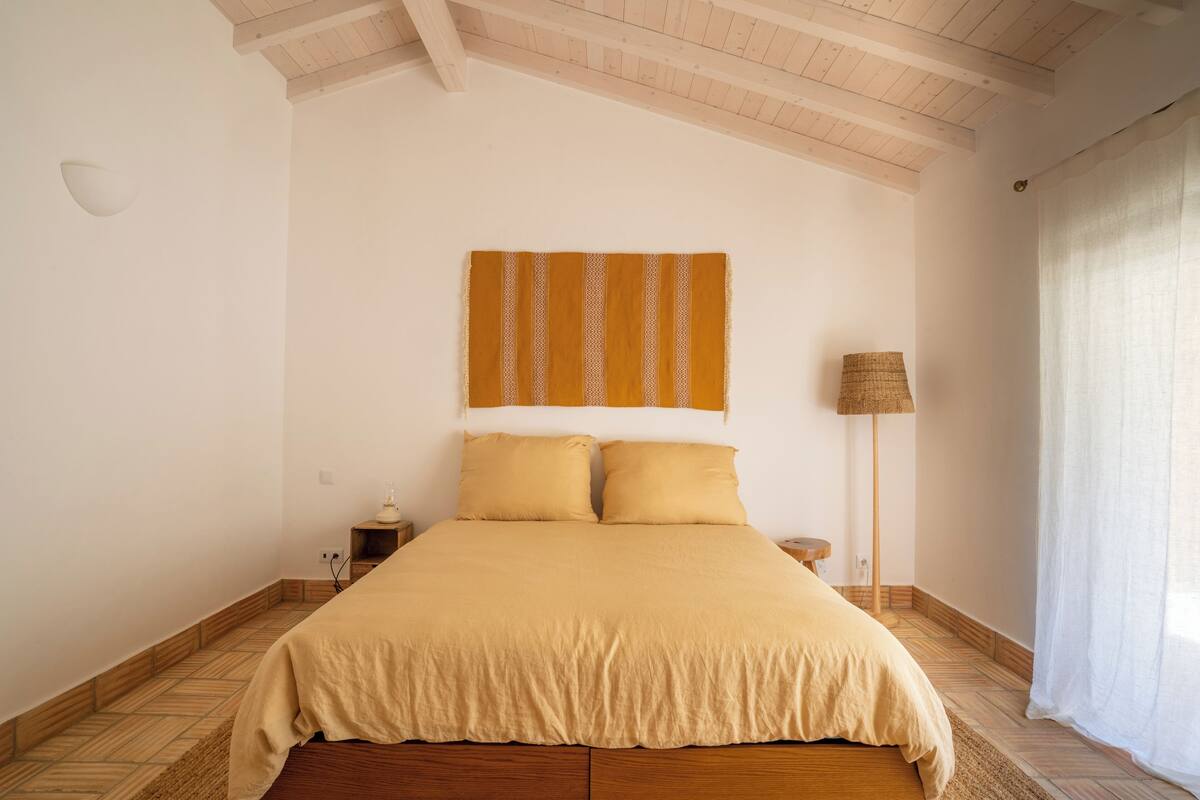 A bedroom with a bed, a nightstand, a lamp, and a window with curtains.
