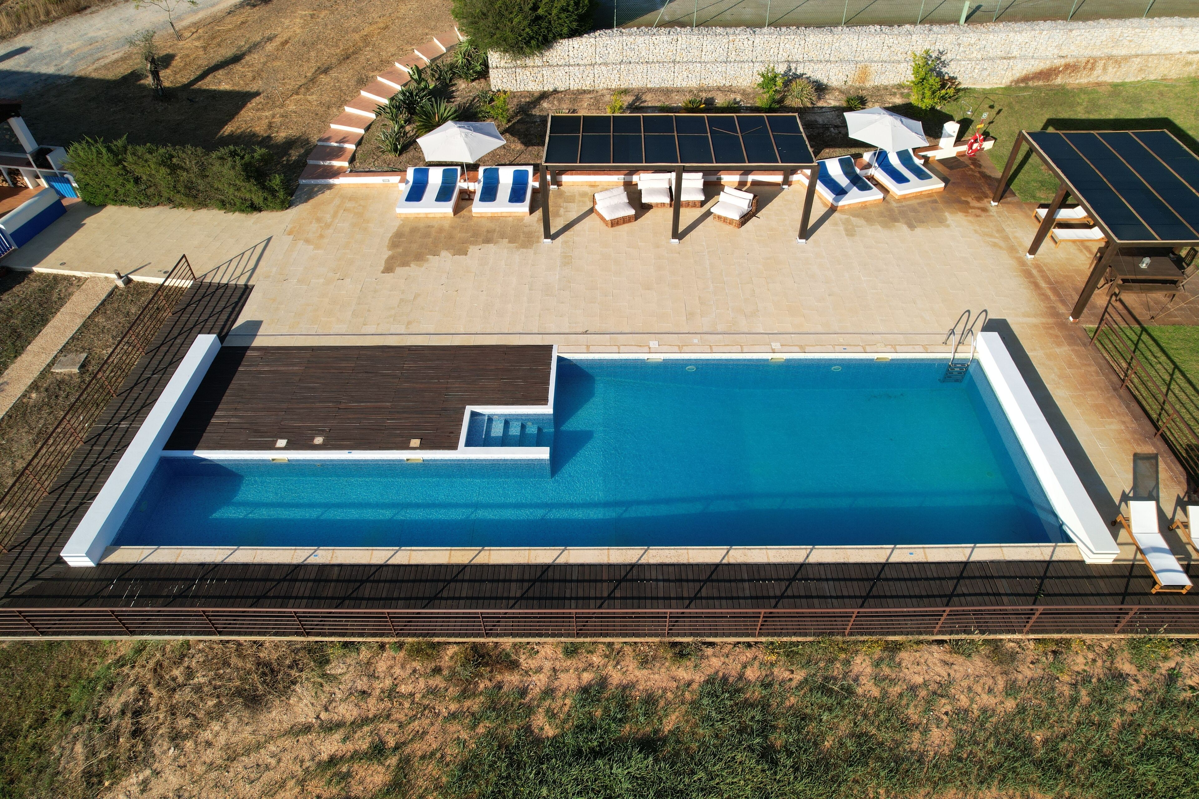 An aerial view of a swimming pool with sun loungers and a covered area with solar panels.