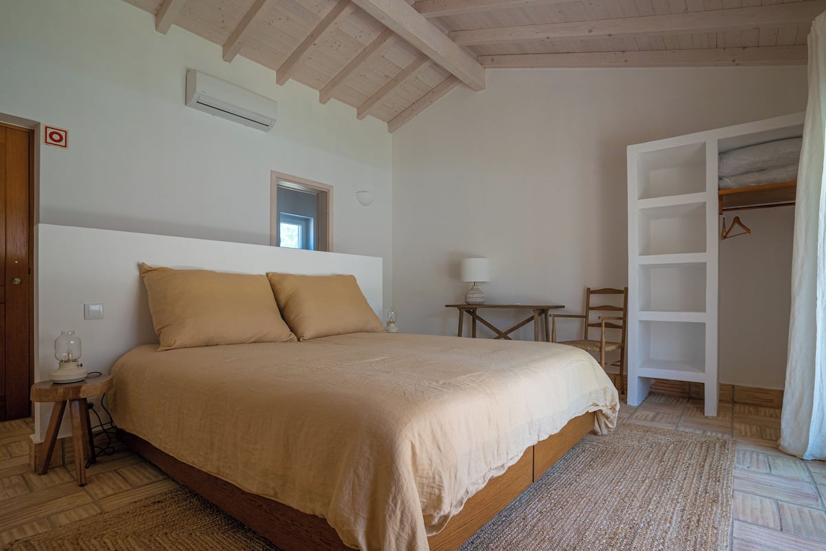A bedroom with a large bed, a bedside table with a lamp, a wooden chair, a wardrobe, and a small table with a lamp.