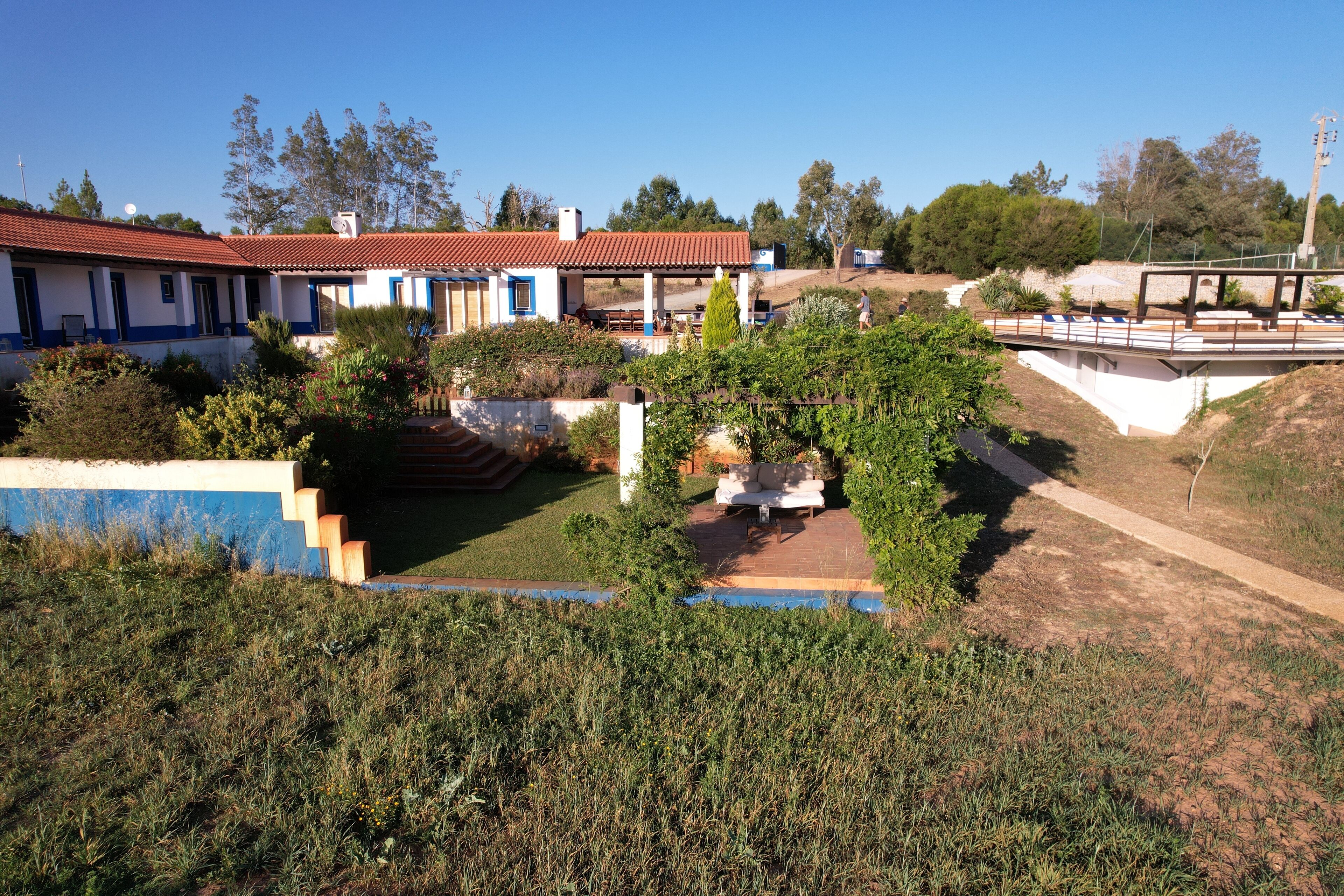 A house with a red-tiled roof, a patio with outdoor furniture, and a staircase leading to the entrance.