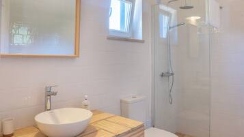 Un baño moderno con un espejo grande, un lavabo de pedestal, un inodoro y una ducha con mampara de vidrio.