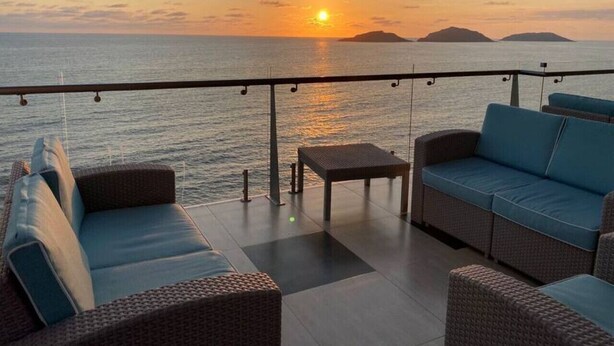 A balcony with wicker furniture and a view of the sunset over the sea.