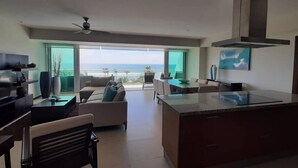 A modern kitchen with a central island, a dining area with a view of the ocean, and a seating area with a sofa and chairs. - Peninsula  Charming and luxury apartment on the beach, with beautiful ocean view (Mazatlán)