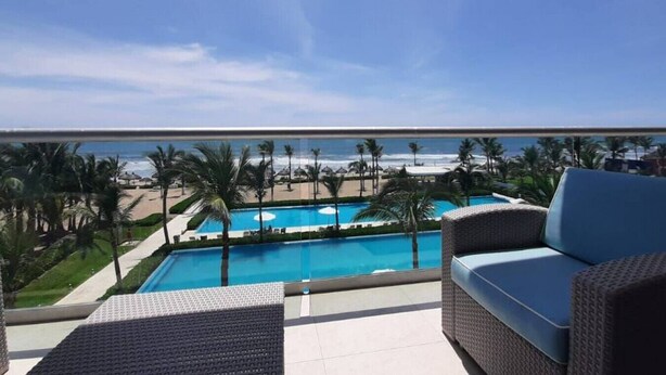 A balcony with a view of a pool and beach, wicker furniture, and a clear sky. - Peninsula  Charming and luxury apartment on the beach, with beautiful ocean view (Mazatlán)