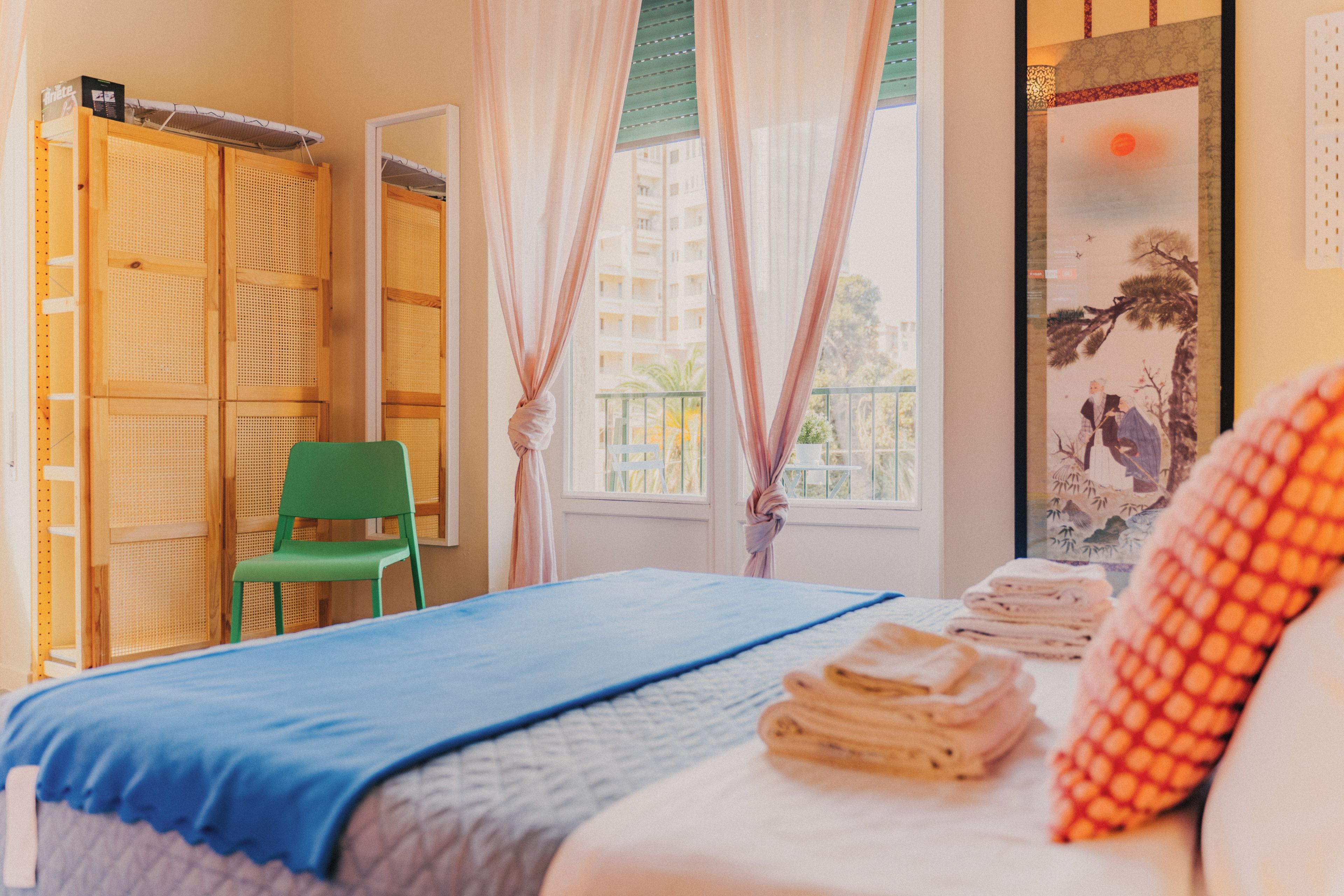 A room with a bed, a green chair, a wardrobe, and a window with curtains.