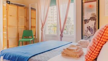 A room with a bed, a green chair, a wardrobe, and a window with curtains.