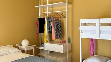 A hotel room with a bunk bed, a desk with a chair, a wardrobe, and a bedside table.