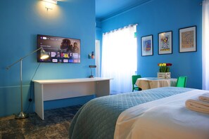 Habitación de hotel con cama, escritorio, televisión mostrando un programa y ventana con cortinas.