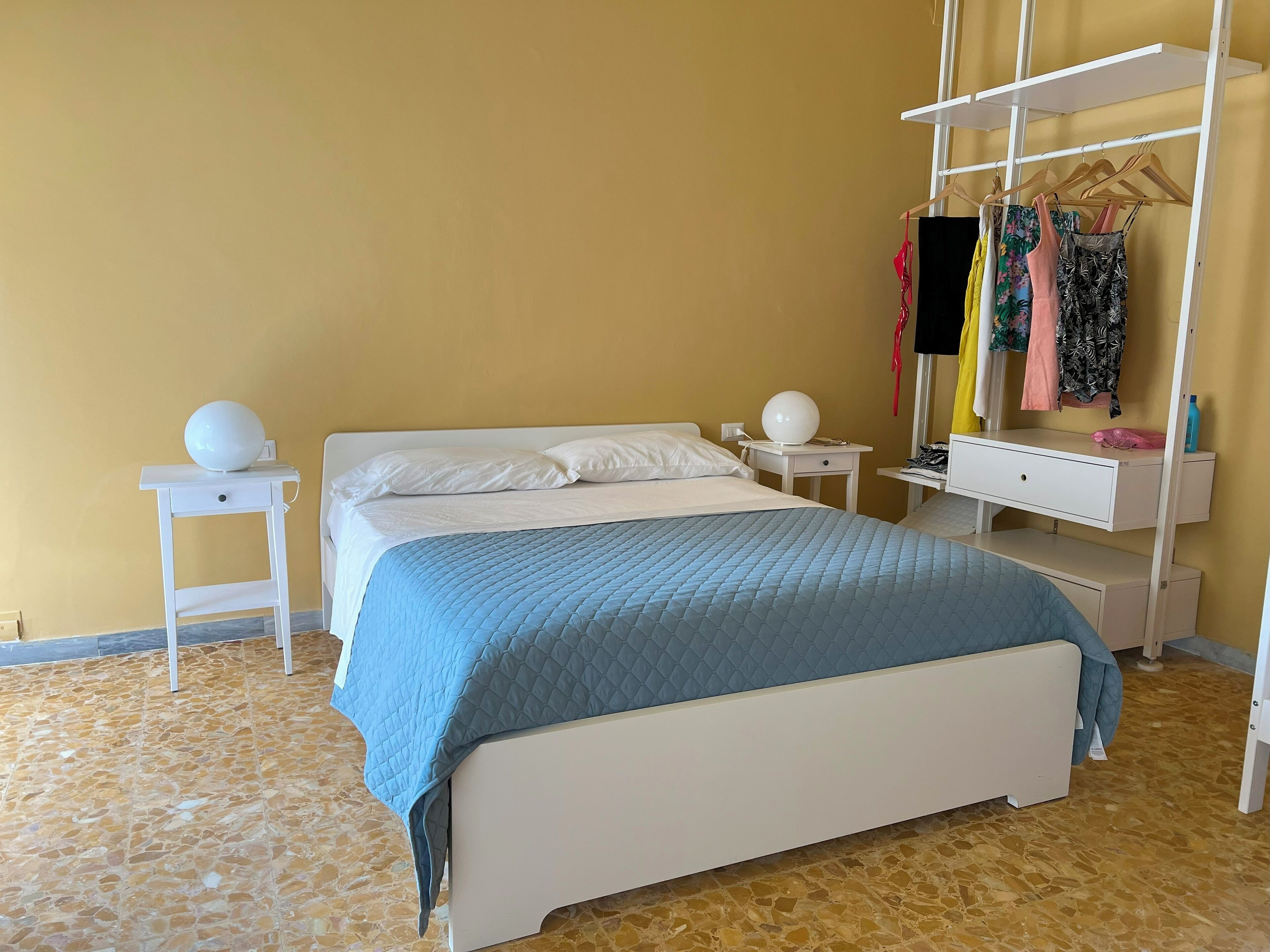A neatly arranged bedroom with a bed, bedside tables, a hanging wardrobe, and a small desk.