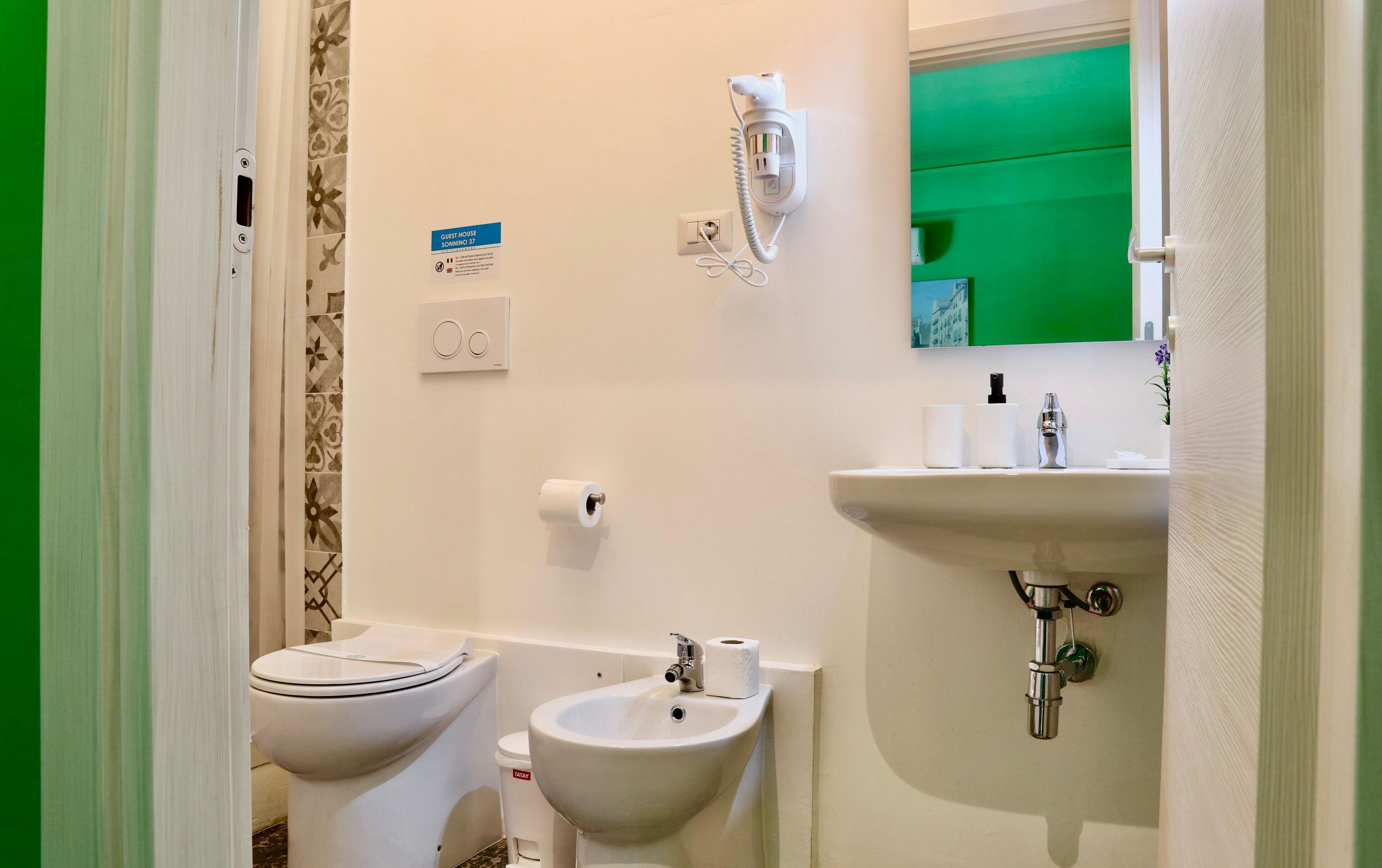 Un baño con inodoro, bidé y lavamanos, una pared verde y un espejo sobre el lavamanos.