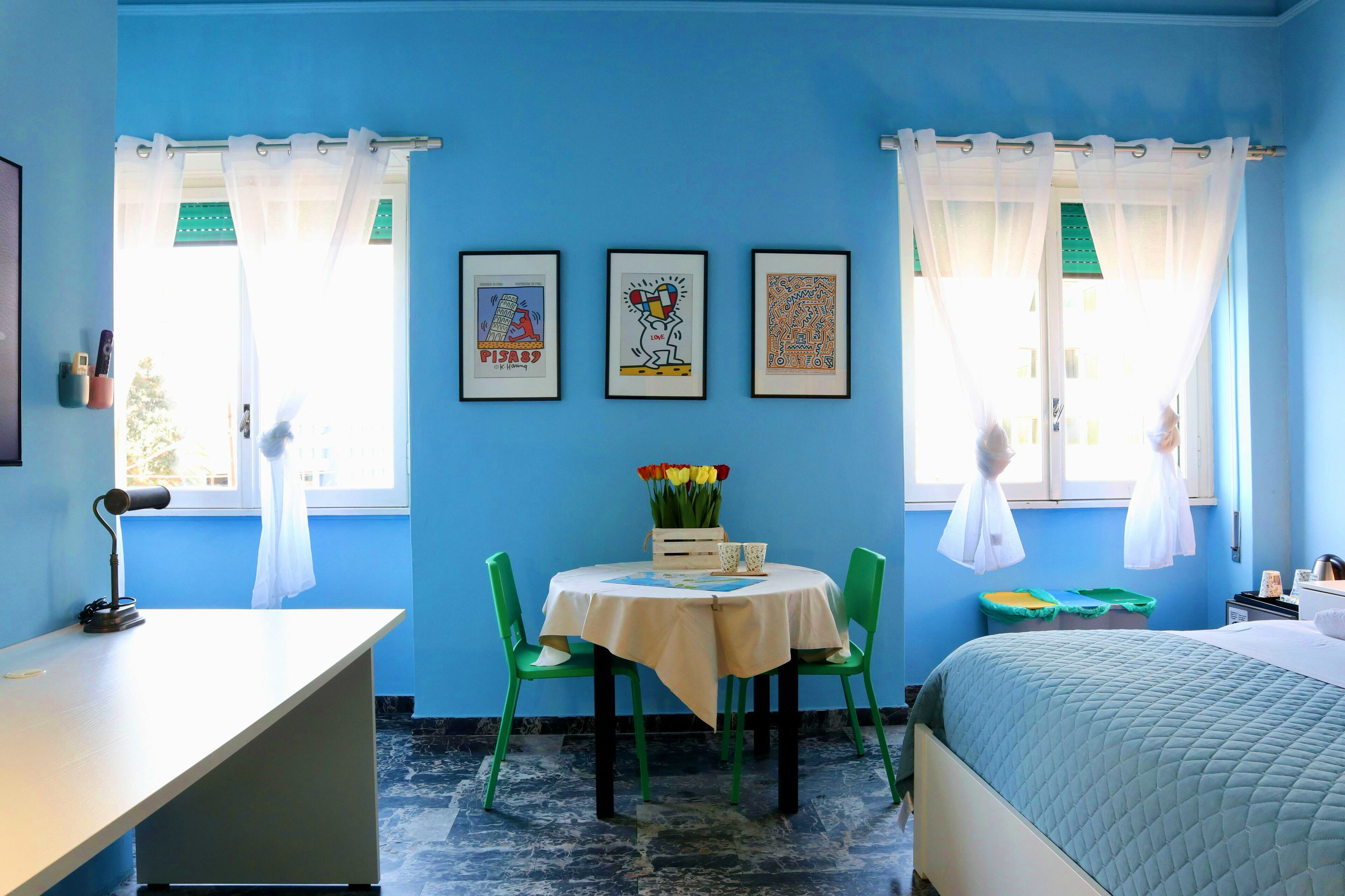 A room with a bed, a desk, and a chair. There are three framed pictures on the wall.