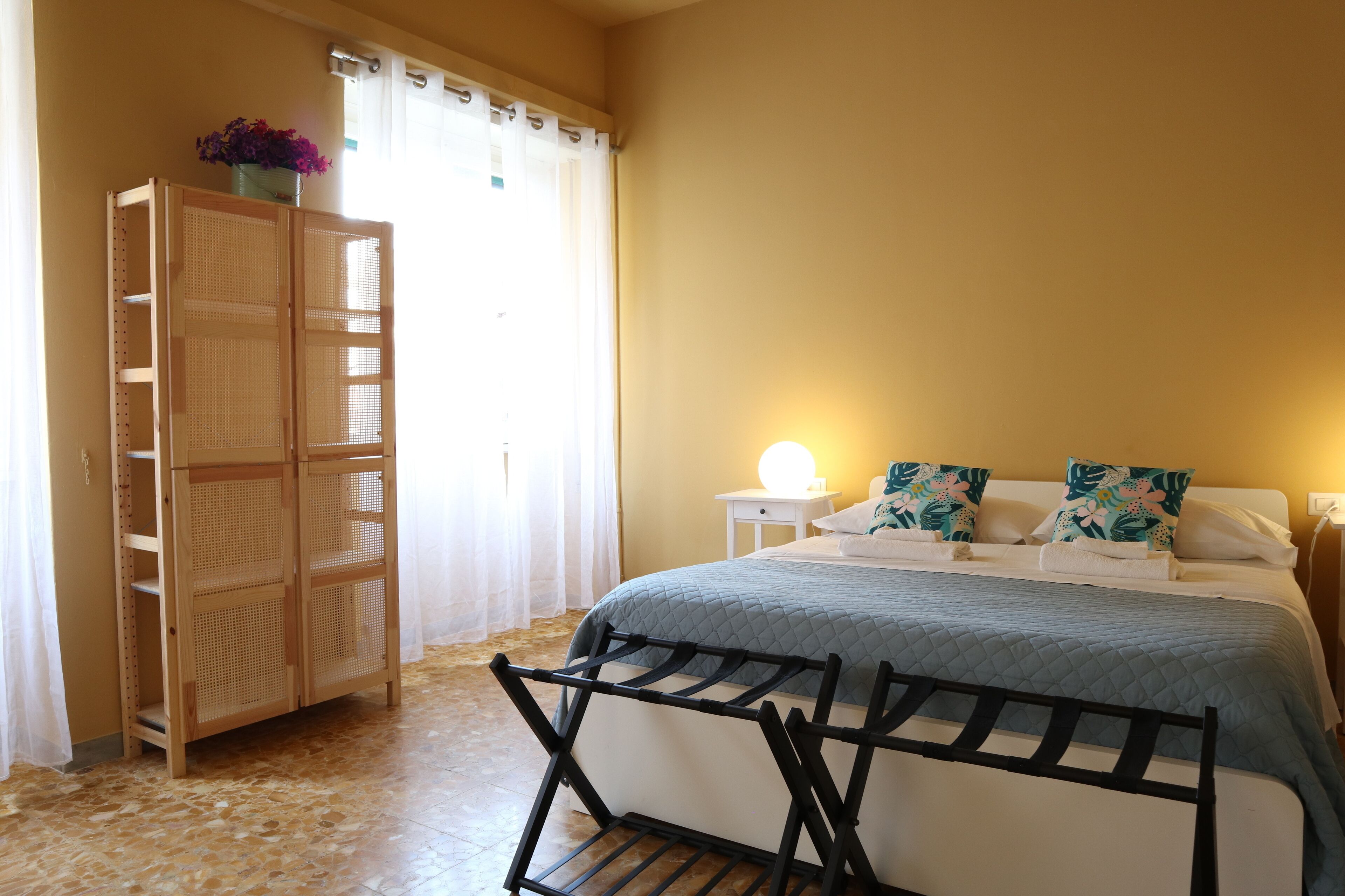 A bedroom with a bed, a bedside table, a lamp, a wardrobe, and a drying rack.