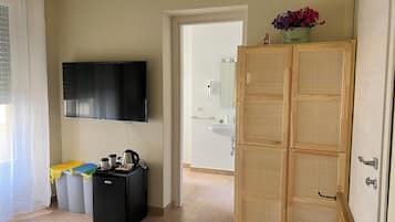 Una habitación con televisión, un refrigerador pequeño negro, un armario de madera y una puerta que da a un baño.