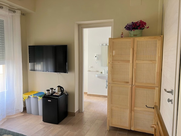 Una habitación con televisión, un refrigerador pequeño negro, un armario de madera y una puerta que da a un baño.