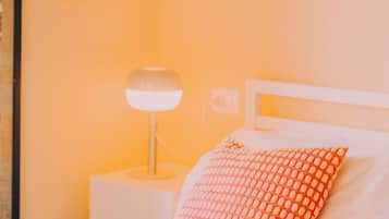 Una cama con cabecera blanca, almohada roja estampada y manta blanca.