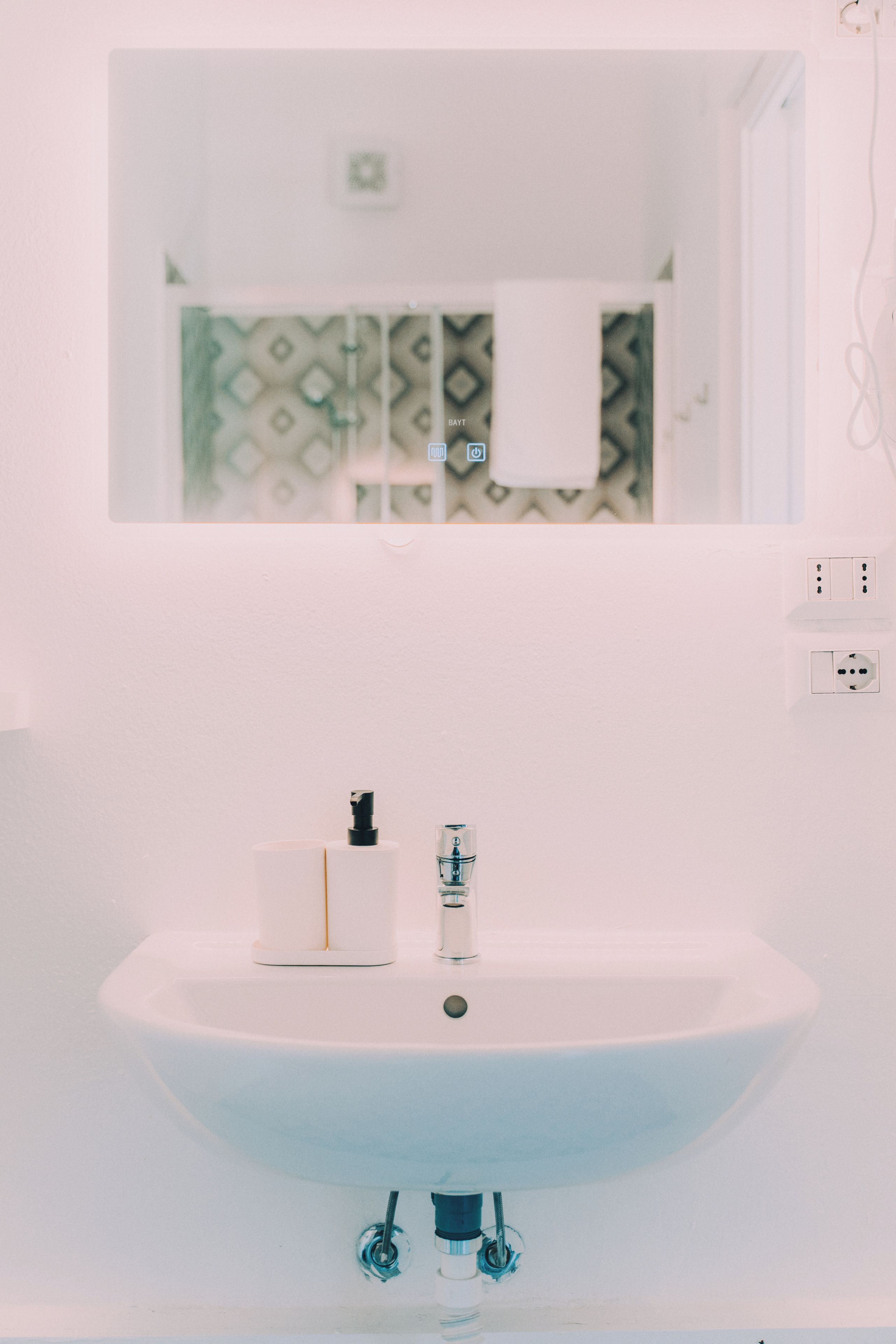 A bathroom with a white sink, a mirror, and a towel hanging on the wall.