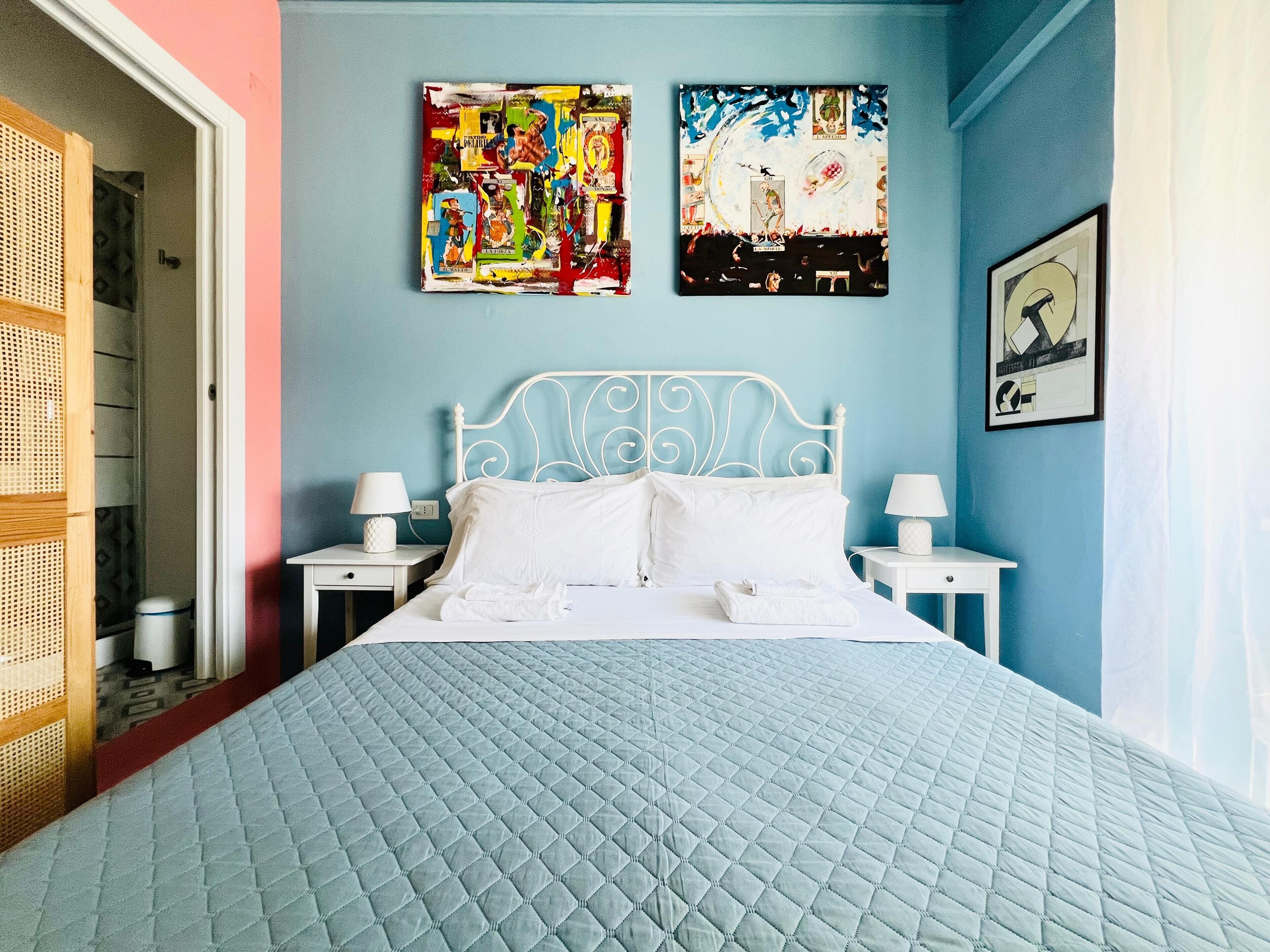 A bedroom with a bed, two bedside tables, and two wall-mounted paintings.
