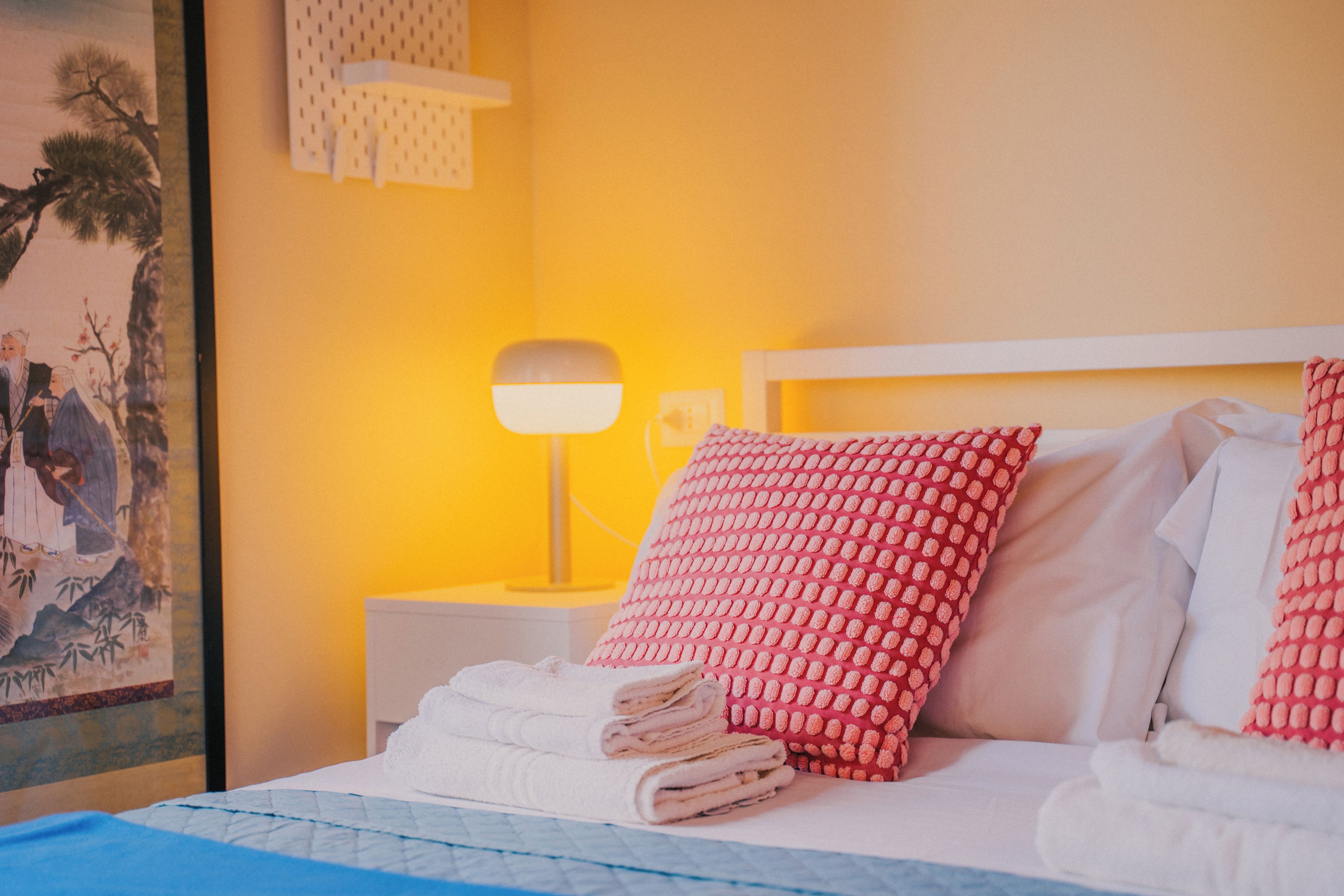 A hotel room with a neatly made bed, a bedside lamp, and a wall with a painting.