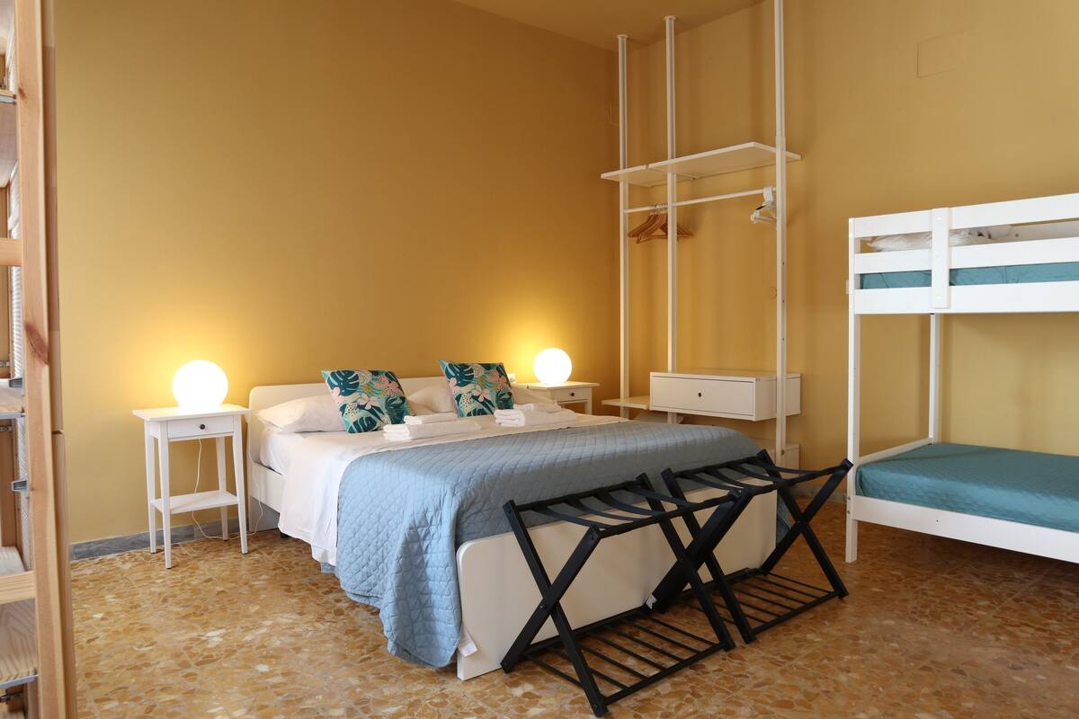 Una habitación con una cama, dos mesitas de noche, una silla colgante y una litera.