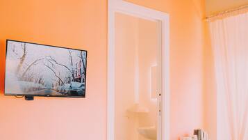 Una habitación de hotel con cama, televisión, armario, escritorio con computadora y baño.