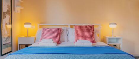 A hotel room with a bed, two bedside lamps, a framed picture on the wall, and a blue bedspread.