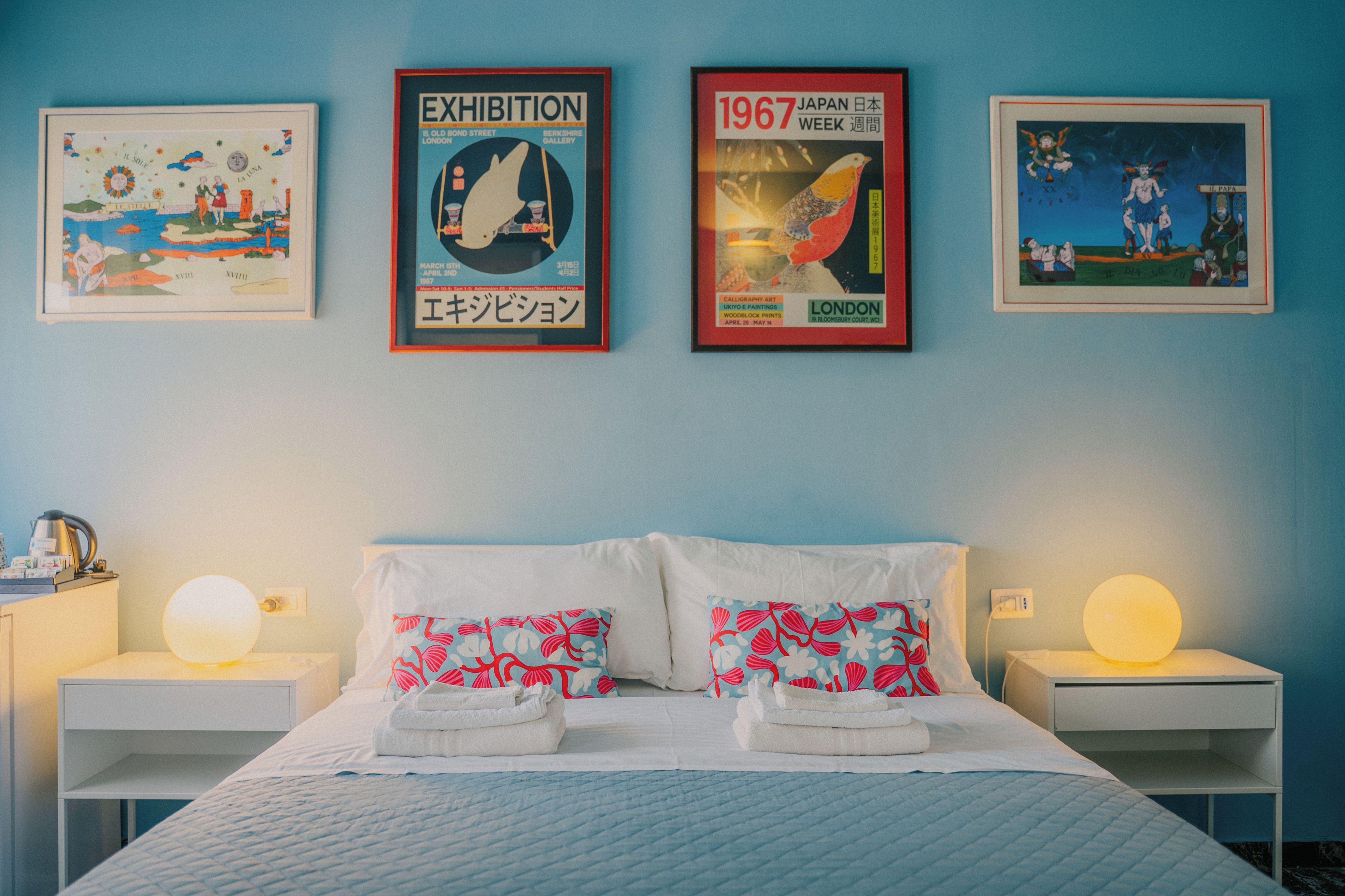 A hotel room with a bed, two nightstands, and three framed artworks on the wall.