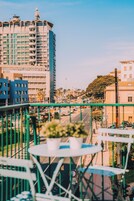 Un balcón con mesa y sillas, con vistas a un paisaje urbano que incluye edificios y una calle.