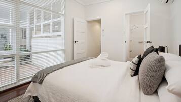 A bedroom with a large bed, a window with blinds, and a door leading to a bathroom.