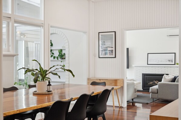 Uma sala de estar moderna com uma mesa de jantar de madeira, cadeiras pretas, uma lareira e uma janela grande.