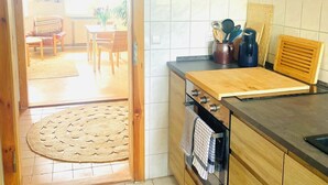 A kitchen with wooden cabinets, a countertop, and a stove. There is a door leading to a dining area with a table and chairs. - "MTS Haus - Zettemin" Family-friendly vacation apartments in Mecklenburg (Zettemin)