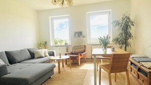 A living room with a grey sofa, wooden dining table, and chairs, a small rug, and a potted plant. - "MTS Haus - Zettemin" Family-friendly vacation apartments in Mecklenburg (Zettemin)
