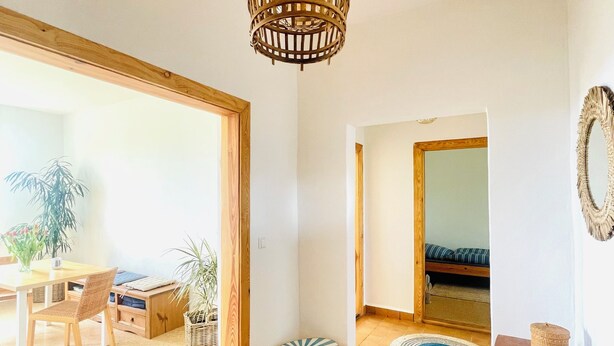 A spacious living area with a wooden dining table, chairs, a woven rug, a hanging light fixture, and a bed in the background. - "MTS Haus - Zettemin" Family-friendly vacation apartments in Mecklenburg (Zettemin)