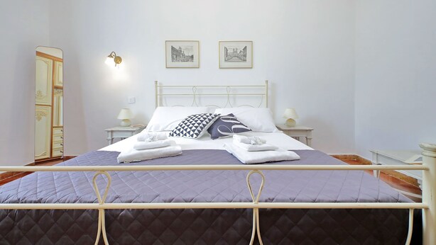 A neatly made bed with a quilted cover, two bedside lamps, and a nightstand with a lamp. - 4bnb - Queen Mary Vatican Home (Rome)