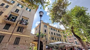 A street scene with a row of buildings, a street lamp, and a market stall. - 4bnb - Queen Mary Vatican Home (Rome)