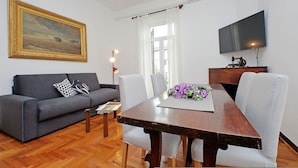 Uma sala de estar com sofá, mesa de jantar, cadeiras, um quadro e televisão.