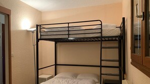 A bunk bed room with a single bed below and a bunk bed above. There is a small bedside table and a lamp on the wall. - Renovated 2P apartment on slopes, quiet, Pra Loup (Pra-Loup)