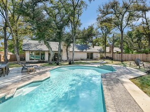 A backyard with a swimming pool, patio furniture, and a house with a stone exterior.