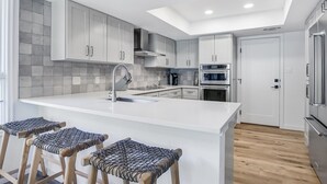 Een moderne keuken met witte kasten, een centraal eiland, barstoelen en inbouwapparatuur.