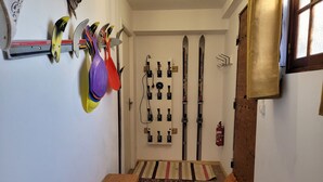 A narrow hallway with skis and ski poles on the wall, a wooden bench, and a patterned rug on the floor.