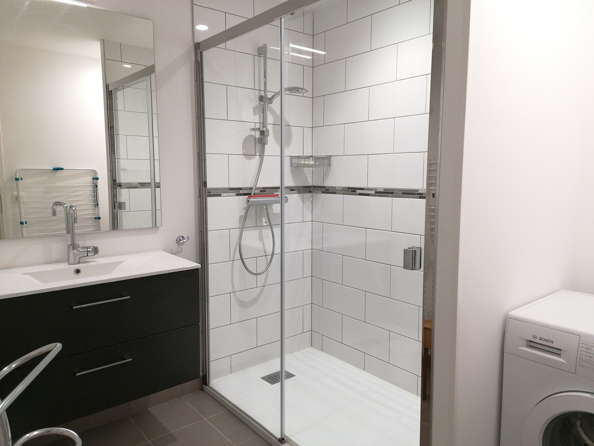 A modern bathroom with a glass-enclosed shower, a sink with a mirror, and a Bosch washing machine.
